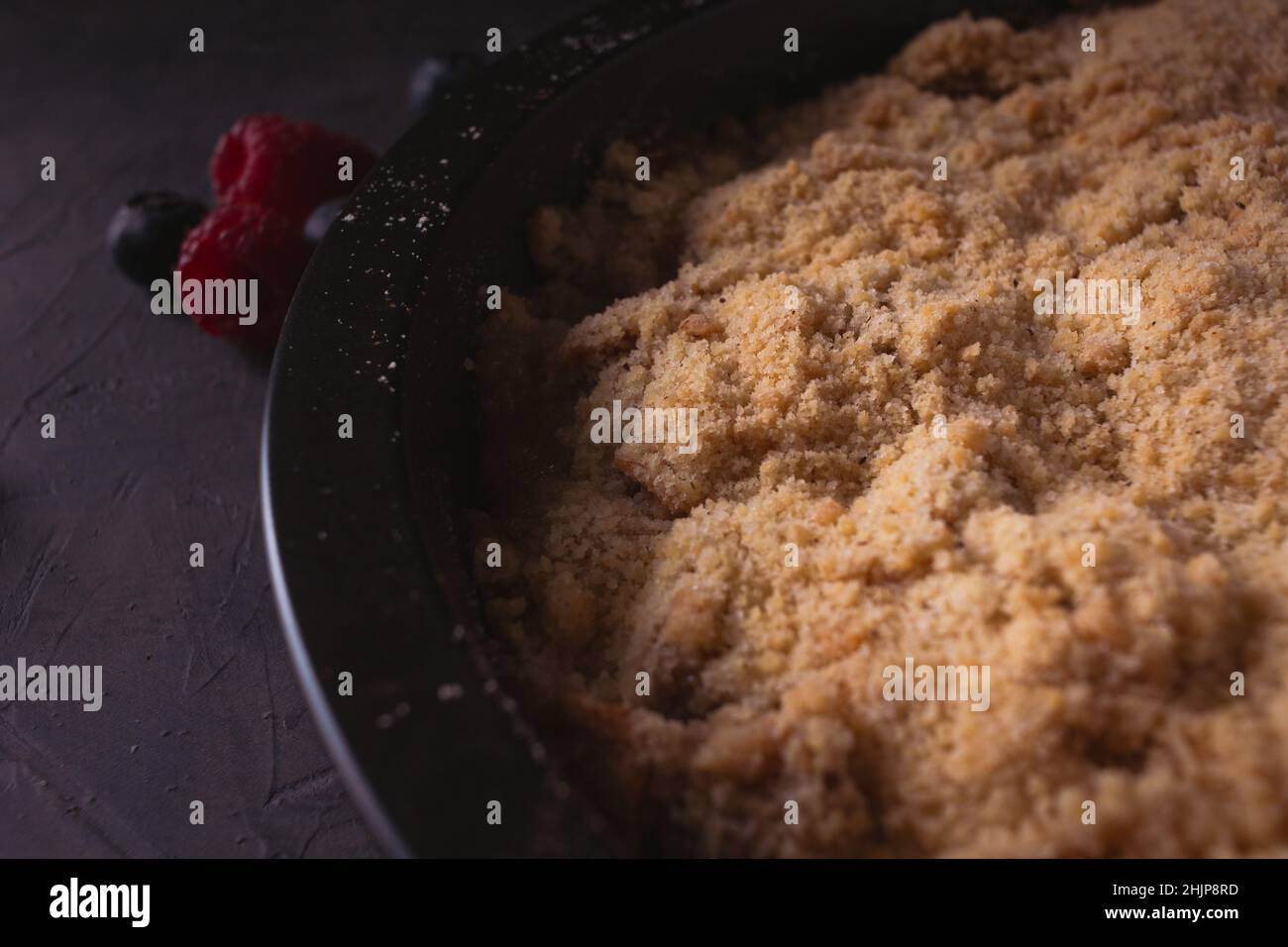 Homemade apple crumble with berries in low light. Dark food photo with copy space. Stock Photo