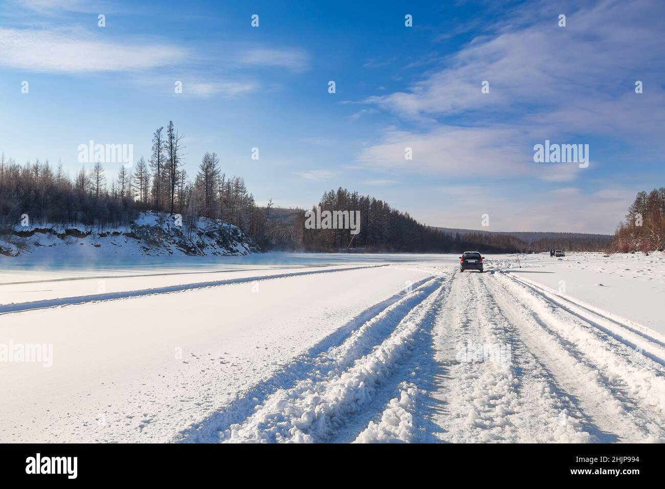 Winter road on the ice of the Chulman River in Yakutia. Landscape of a frozen river and cars on it Stock Photo