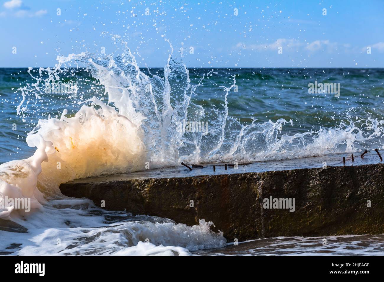 Sea wave splashing when hit at large stony concrete block Stock Photo