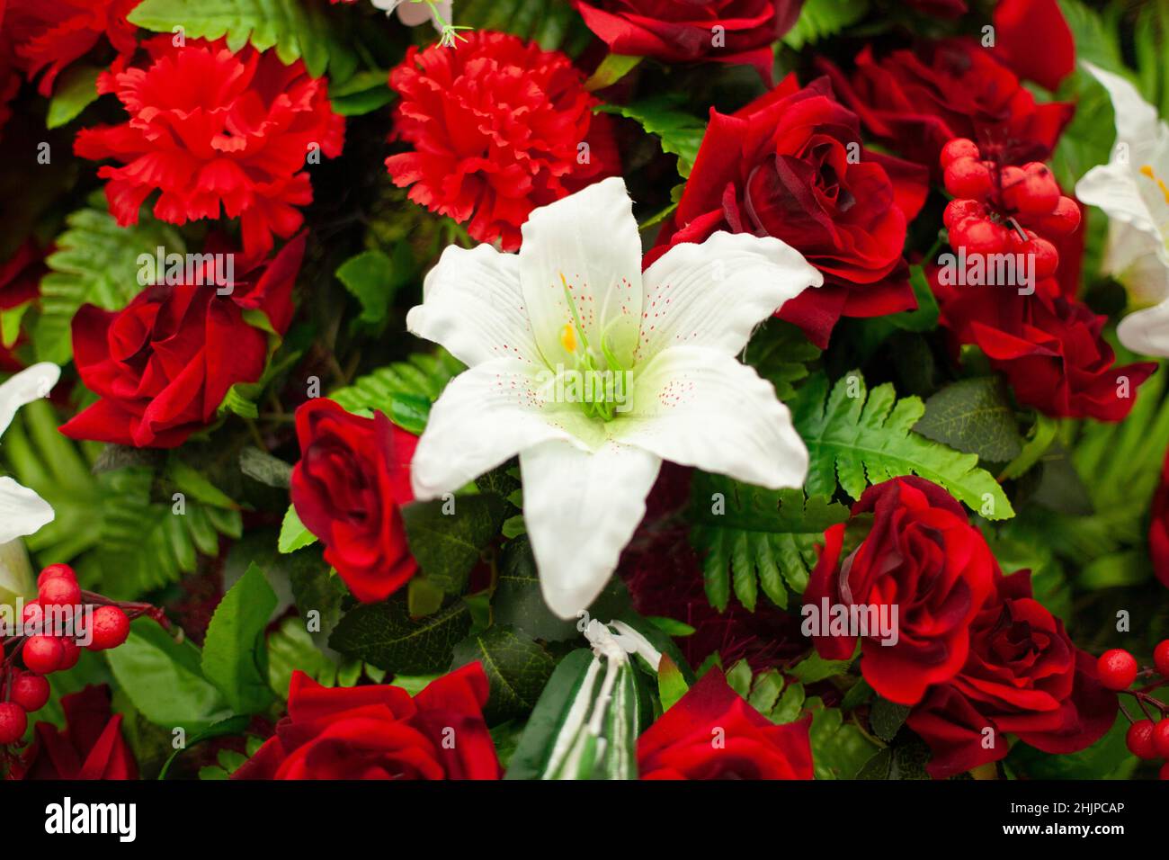 Flowers on monument. Artificial flowers on memorial. Solemn wreath on day of mourning. Funeral decoration. Stock Photo