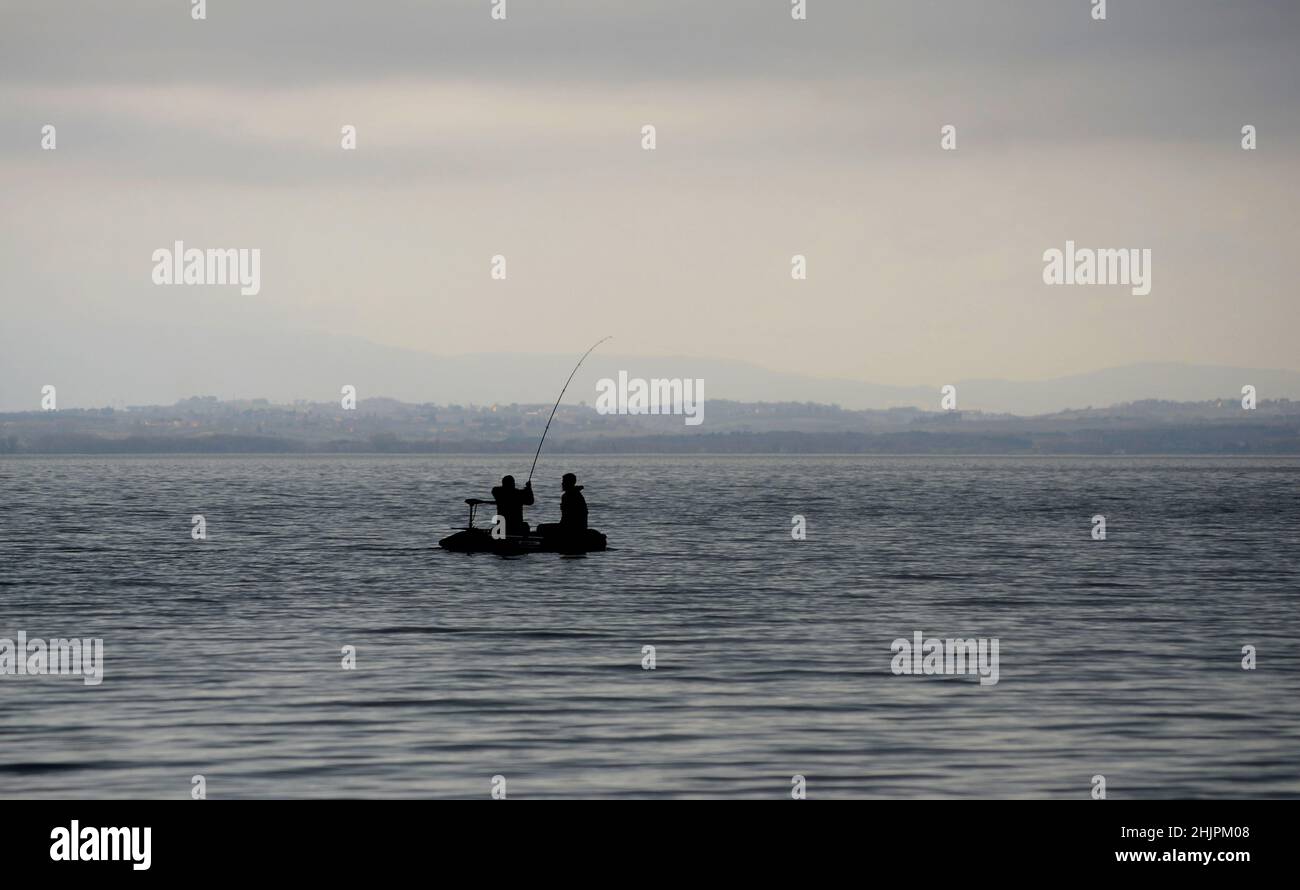 Two Men in a small boat fishing in calm lake on a cloudy winter day Stock Photo