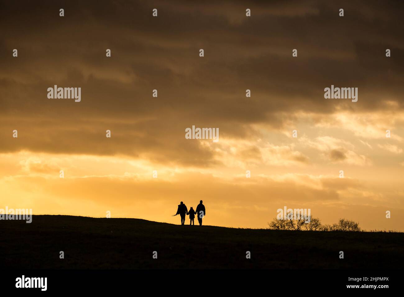 Silhouette of a young family walking isolated into the winter sunset on a hillside in UK countryside. Stock Photo