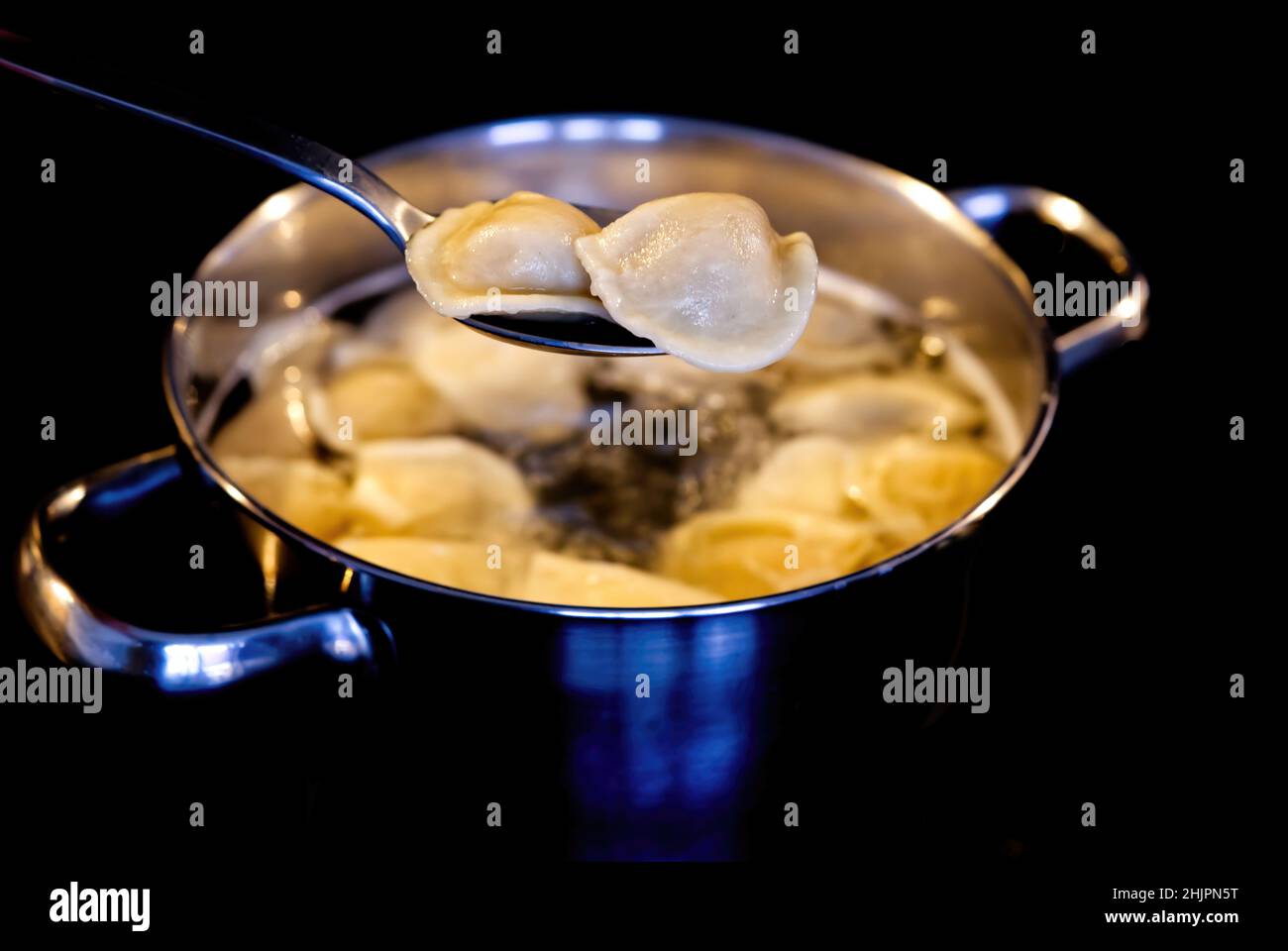 Dumplings mixed with a spoon in a pot of boiling water. Boiled dumplings in a pan. black background Stock Photo