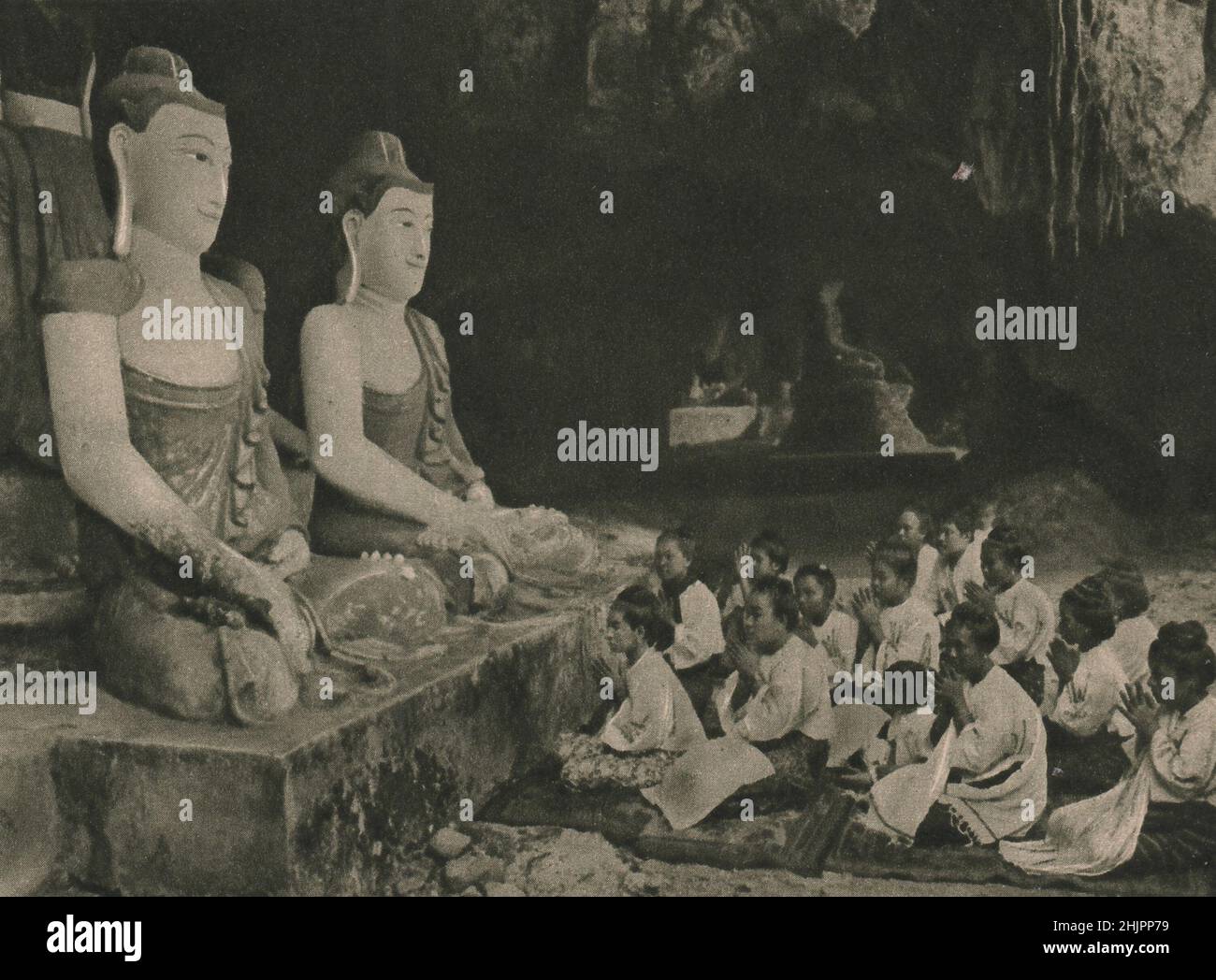 Numerous sitting figures of Buddha of varying sizes still remain in the Moulmein caves, and before them Burmese women pray. Burma (1923) Stock Photo