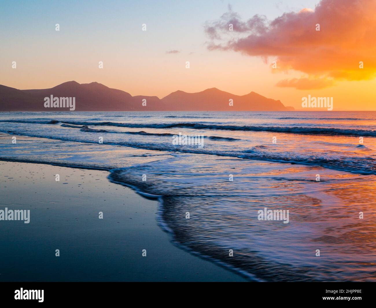 Shoreline on empty beach at low tide with Llyn Peninsula in silhouette at sunset. Dinas Dinlle, Gwynedd, North Wales, UK, Britain Stock Photo