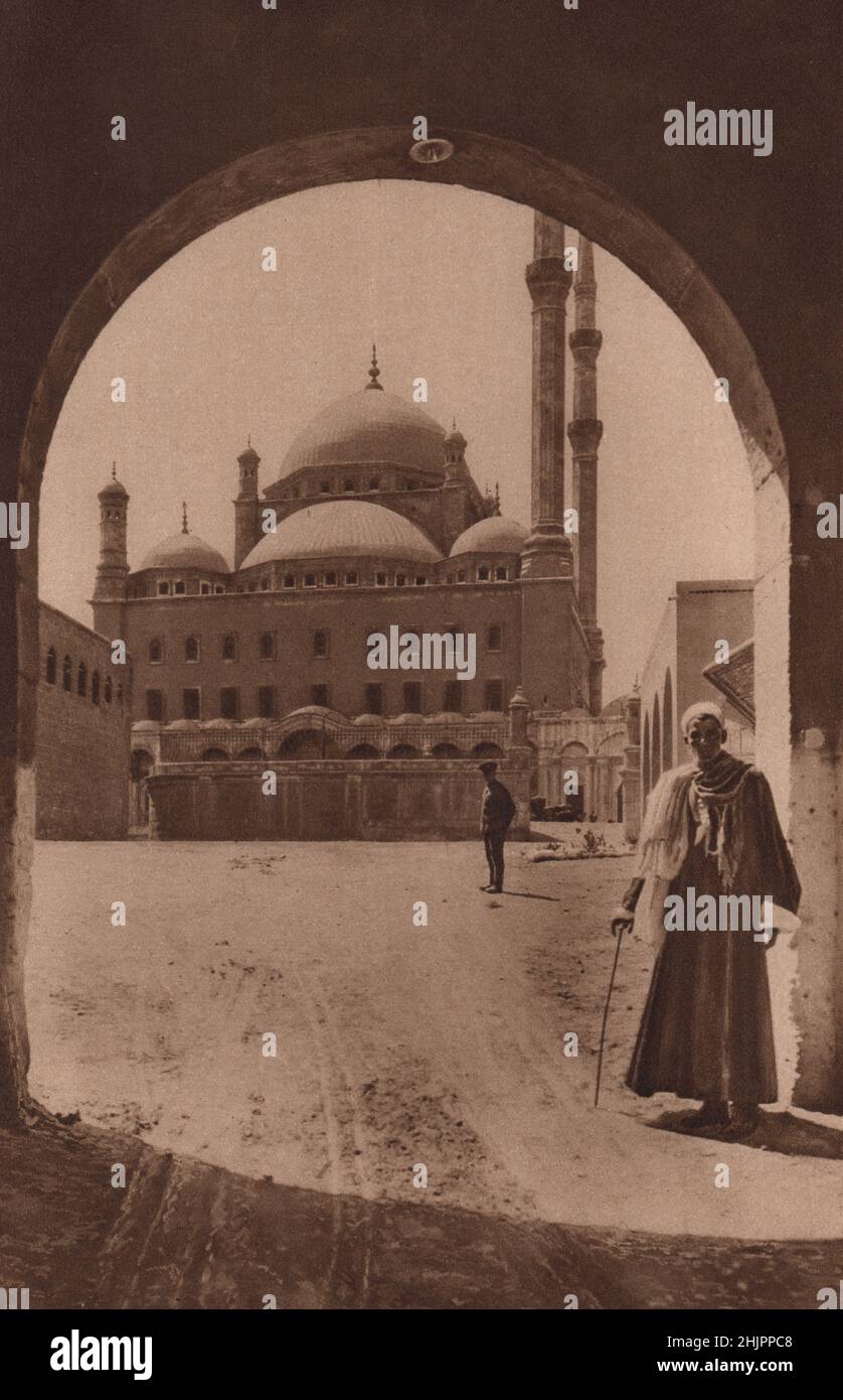 Slender minarets, visible for miles, grace the alabaster Mosque of Mehemet Ali here seen framed in an arch of the Citadel. Egypt. Cairo (1923) Stock Photo