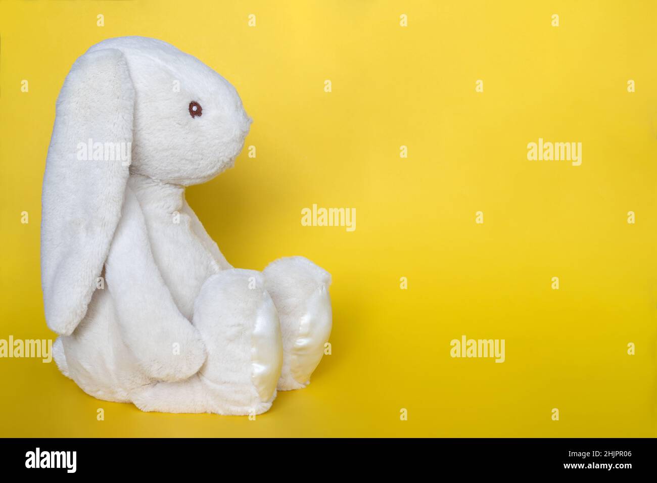 Stuffed bunny on yellow background. Easter concept. Beautisul white toy bunny sitting on colored background with copy space for text Stock Photo