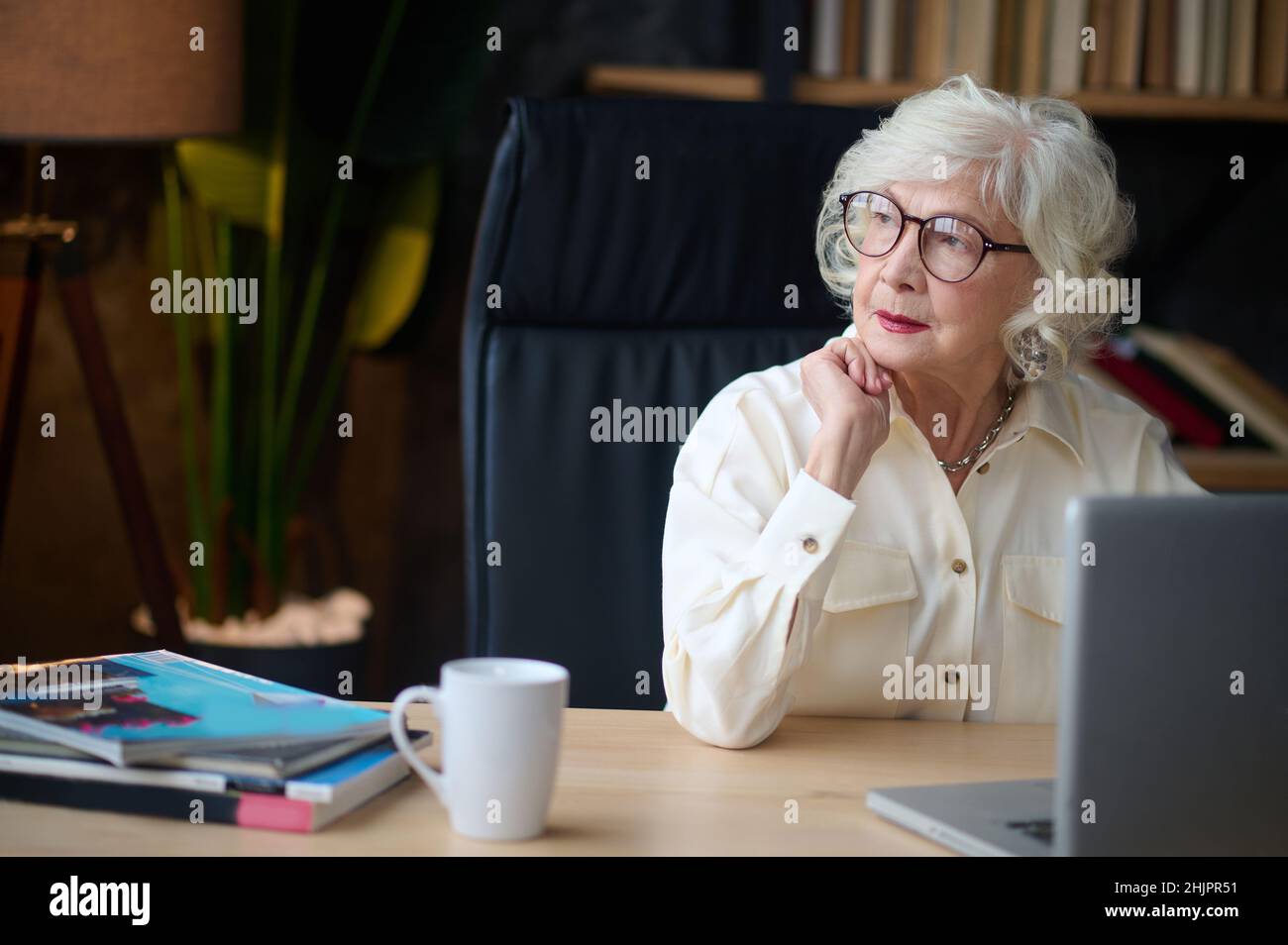 Woman looking away thoughtfully sitting near laptop Stock Photo