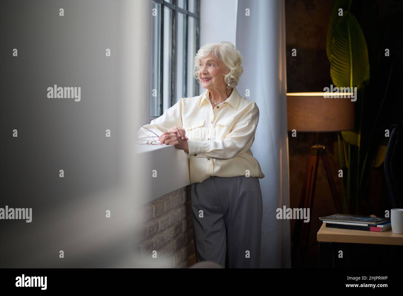 Woman standing near window meditating smiling Stock Photo