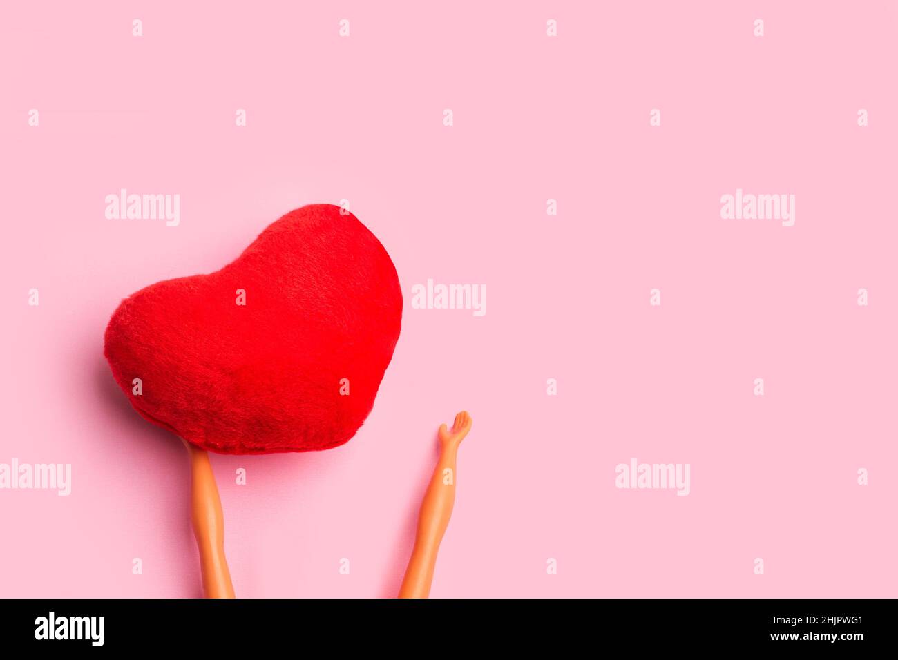 Doll hands holding a textile red heart on a pink background with copy ...