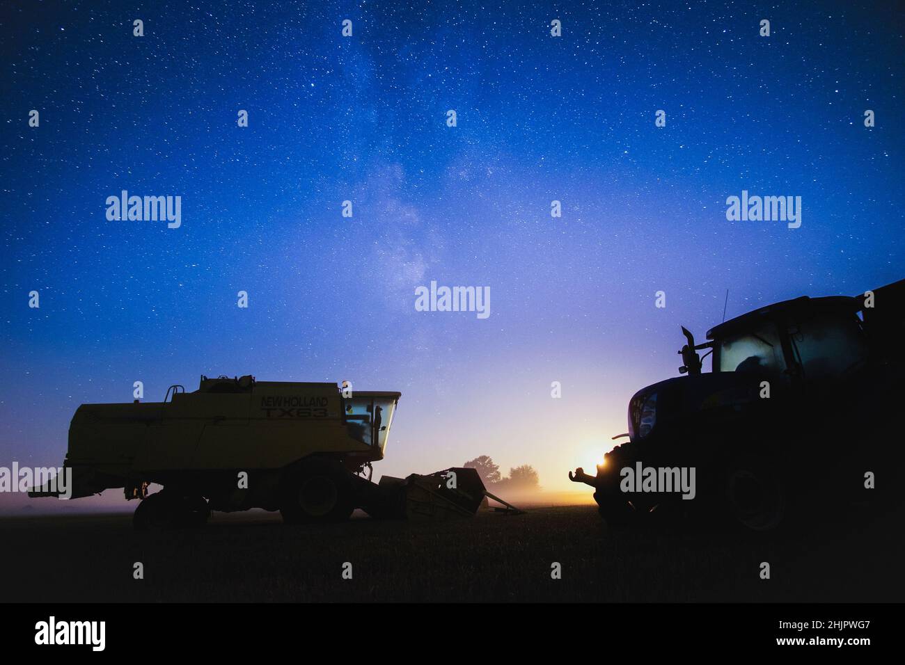 Combine harvester and tractor at night with starry sky and setting moon  Norfolk UK Stock Photo