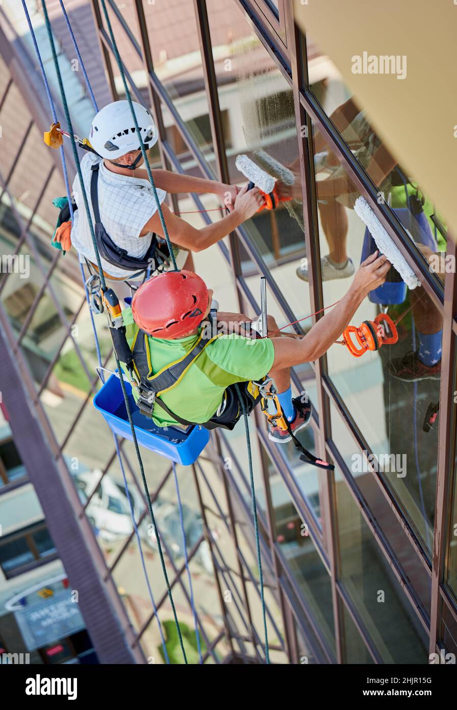 Industrial mountaineering workers washing glass windows of highrise