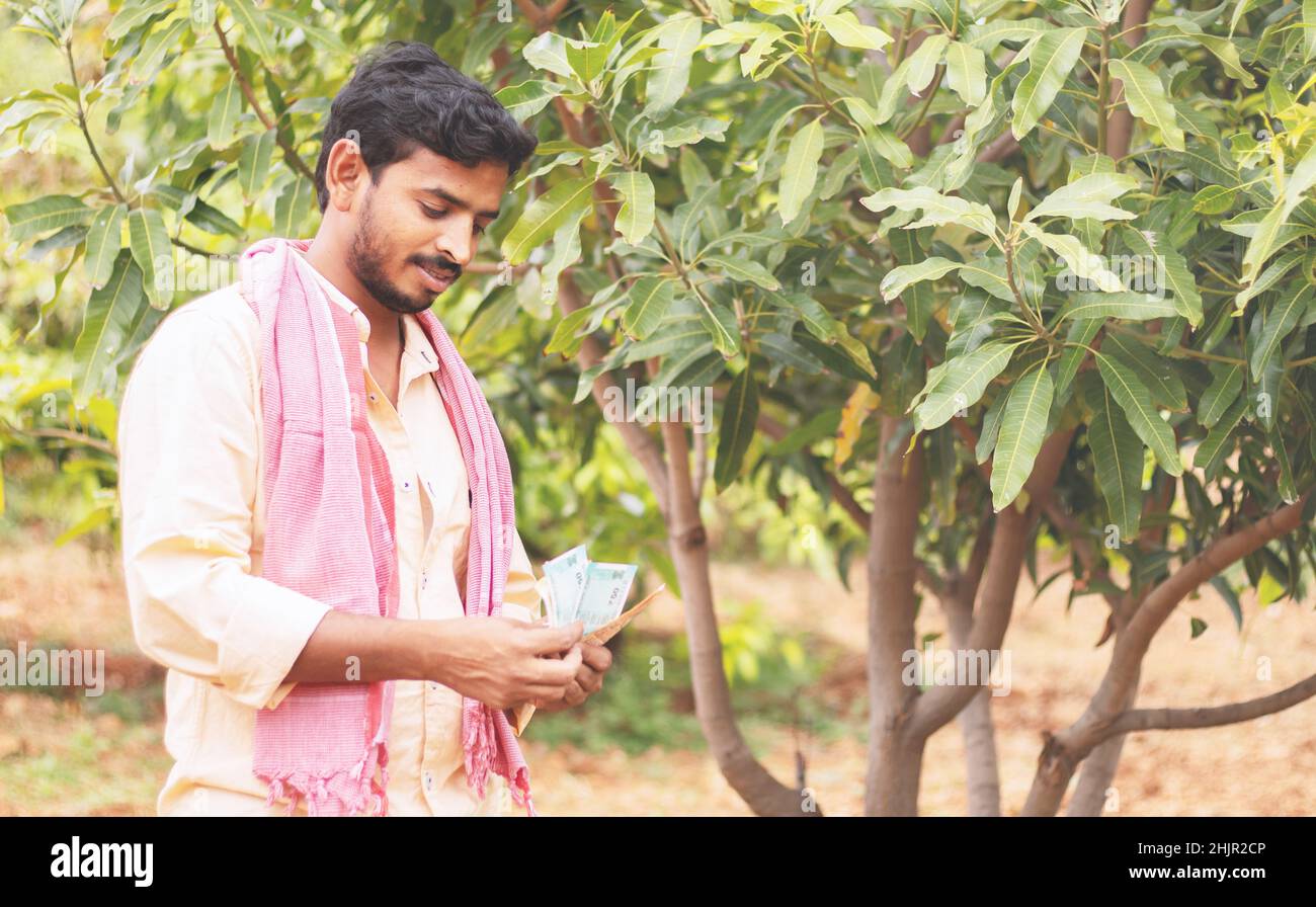 happy young indian former counting money at farm land concept of