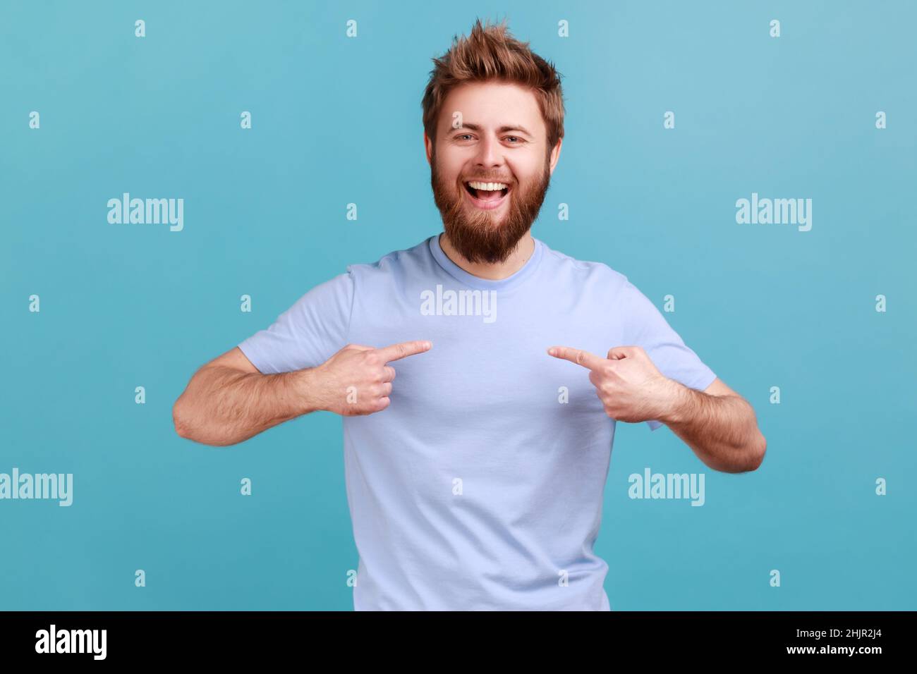 It's me. Portrait of ambitious bearded man with toothy smile, pointing fingers on himself, being confident and proud of his success and achievements. Indoor studio shot isolated on blue background. Stock Photo