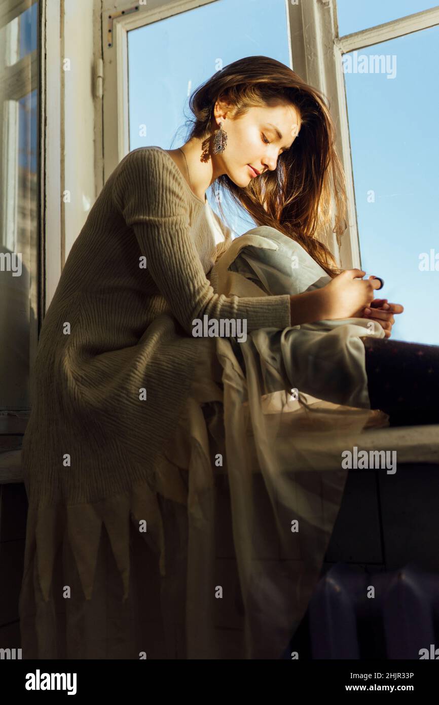 Woman sitting on the windowsill in a dress Stock Photo - Alamy