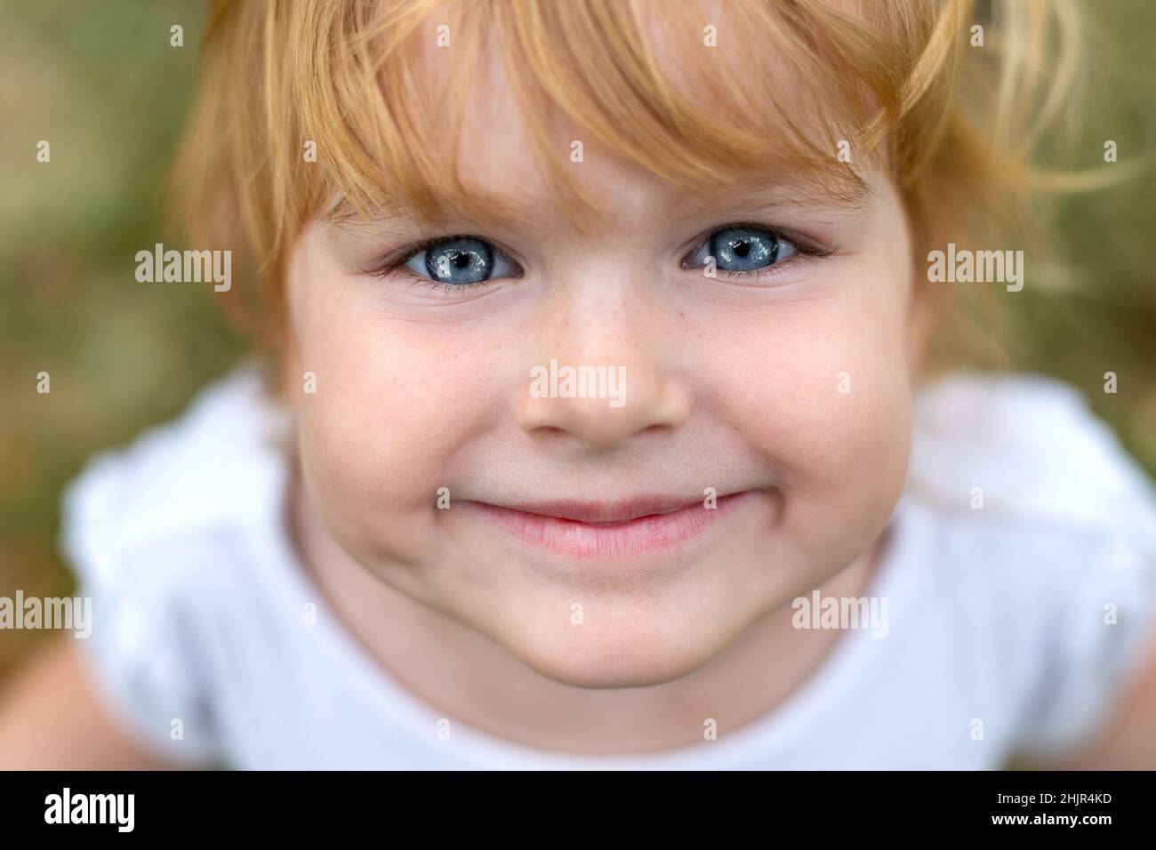 Happy smiling child face close up. Beautiful happy girl with blue eyes and blonde hair. Cute little kid smiling in a park, looking straight in camera Stock Photo