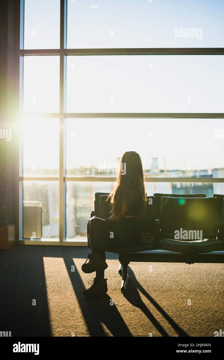 Young Solo Woman waiting at empty airport during golden hour Stock Photo