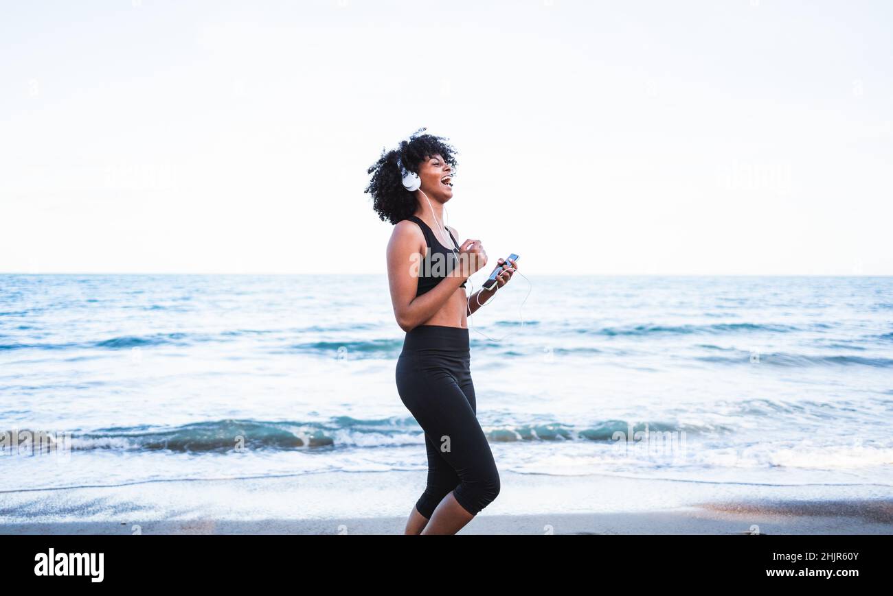 black woman laughing and having fun listening to music on the beach ...