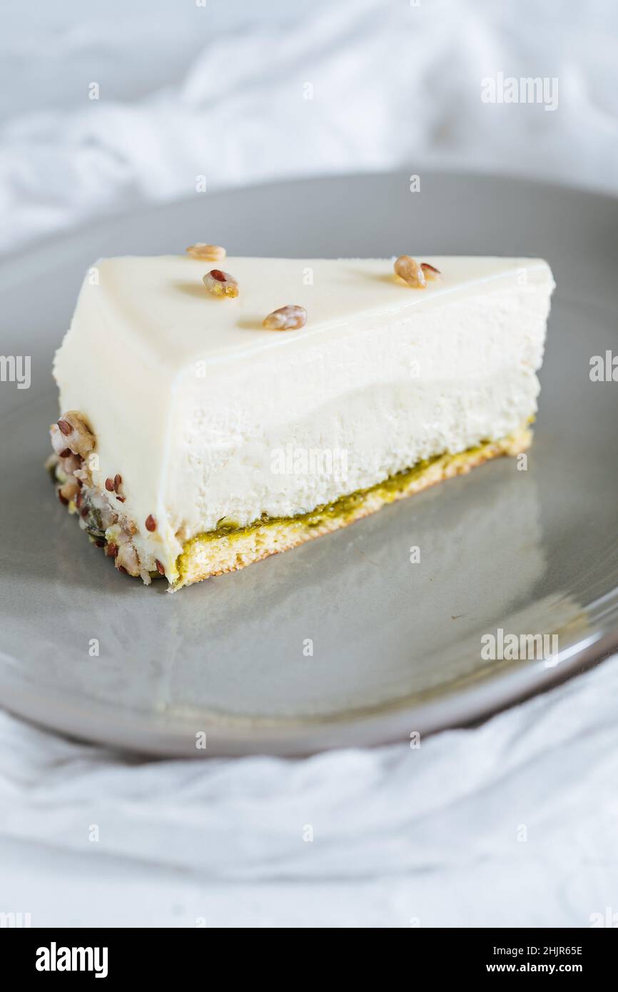 Four layer cake with pistachio, vanilla and white chocolate on grey plate with pistachios on top Stock Photo