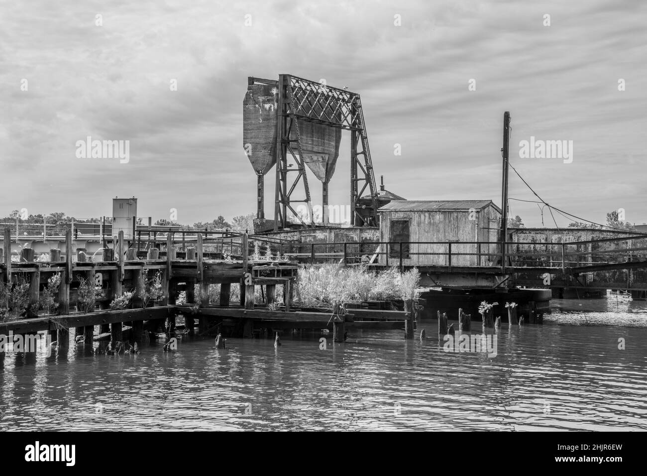 An old bascule railroad bridge (also referred to as a drawbridge or a lifting bridge) on a gray day with a counterweight. In black and white. Stock Photo