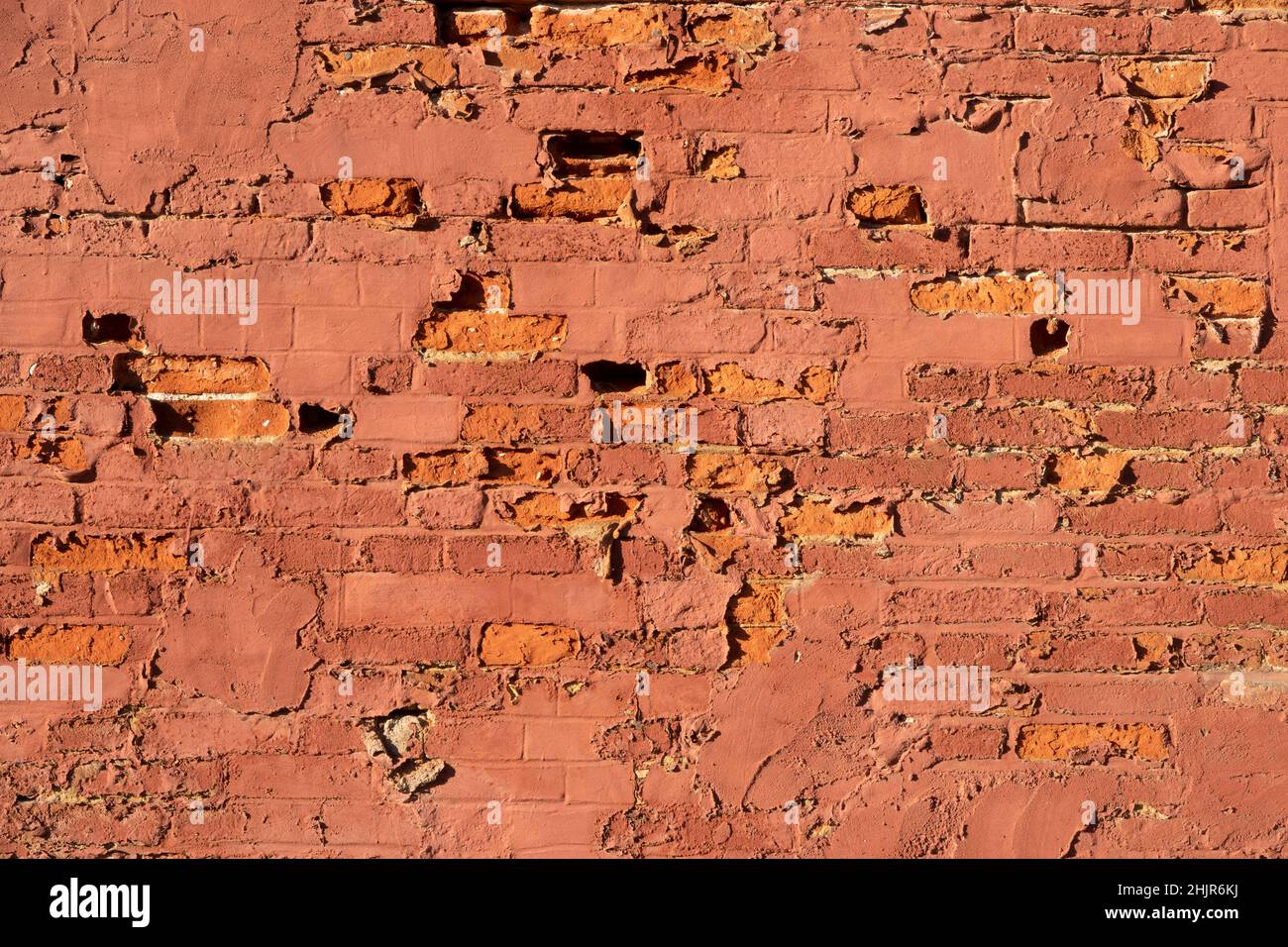 Flaking red paint on a brick wall with many corroded and crumbling