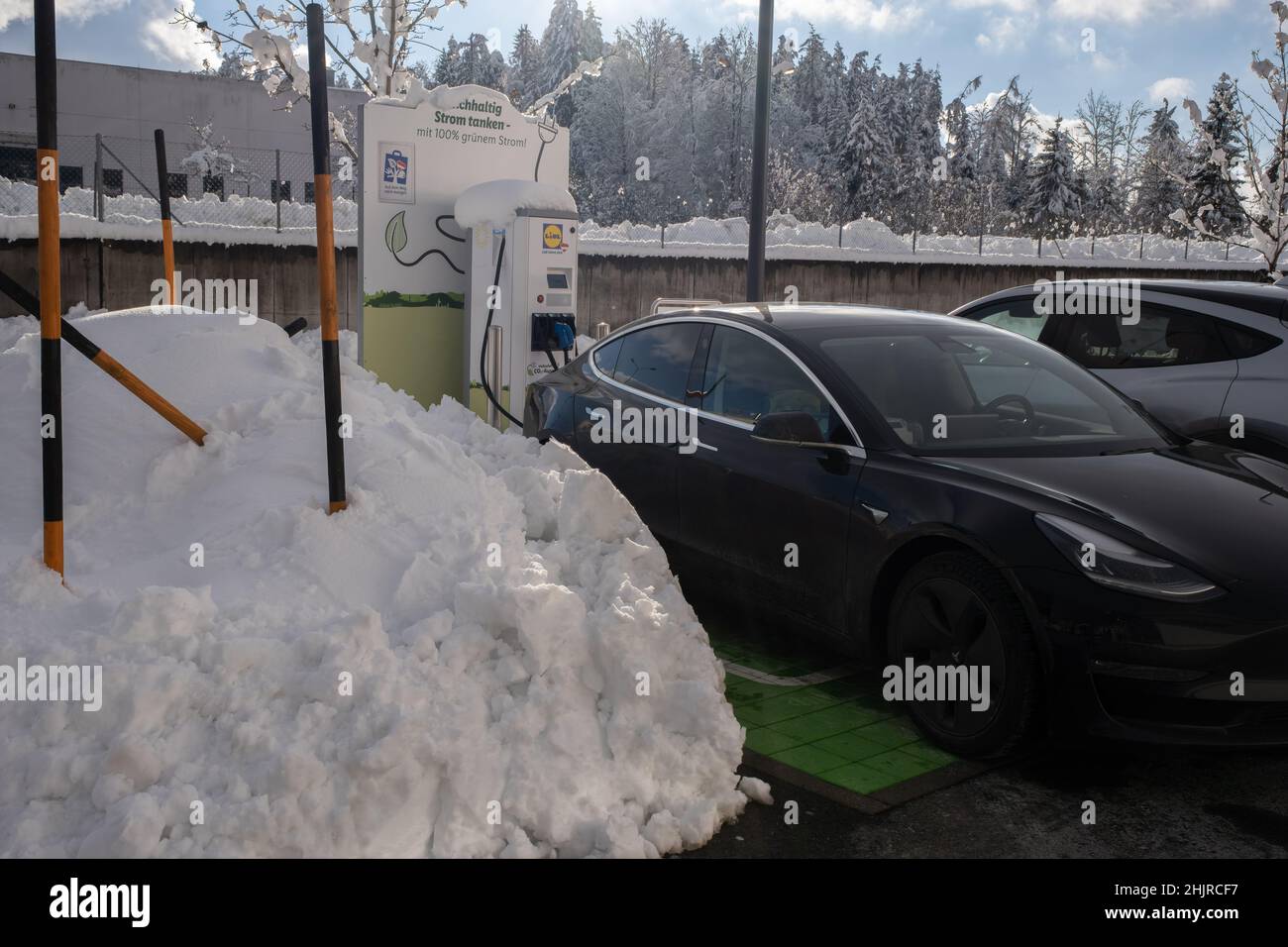 Wernberg, Austria - January 7, 2022. A static shot of a solid black Tesla Model 3 dual motor charging at the LIDL supermarket DC charging station in a Stock Photo
