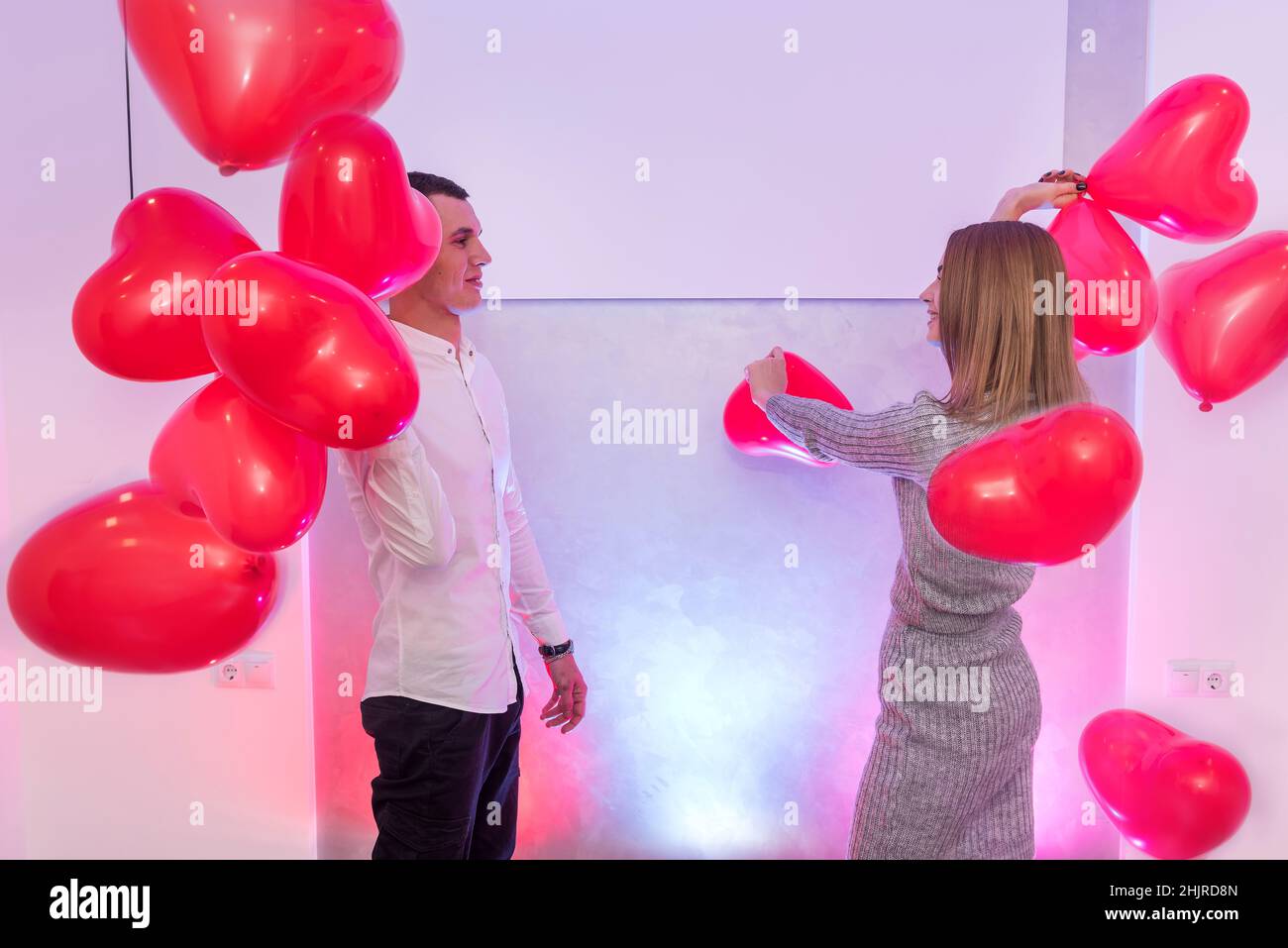 Beautiful couple with red air balloons celebrating Valentine's Day posing in studio Stock Photo