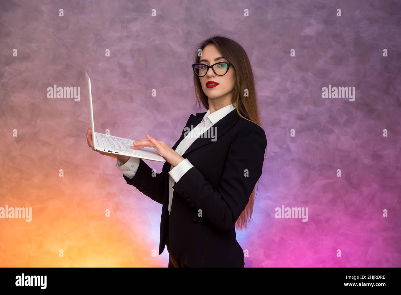 Attractive woman holding white laptop. Secretary or student or teacher posing on abstract background Stock Photo