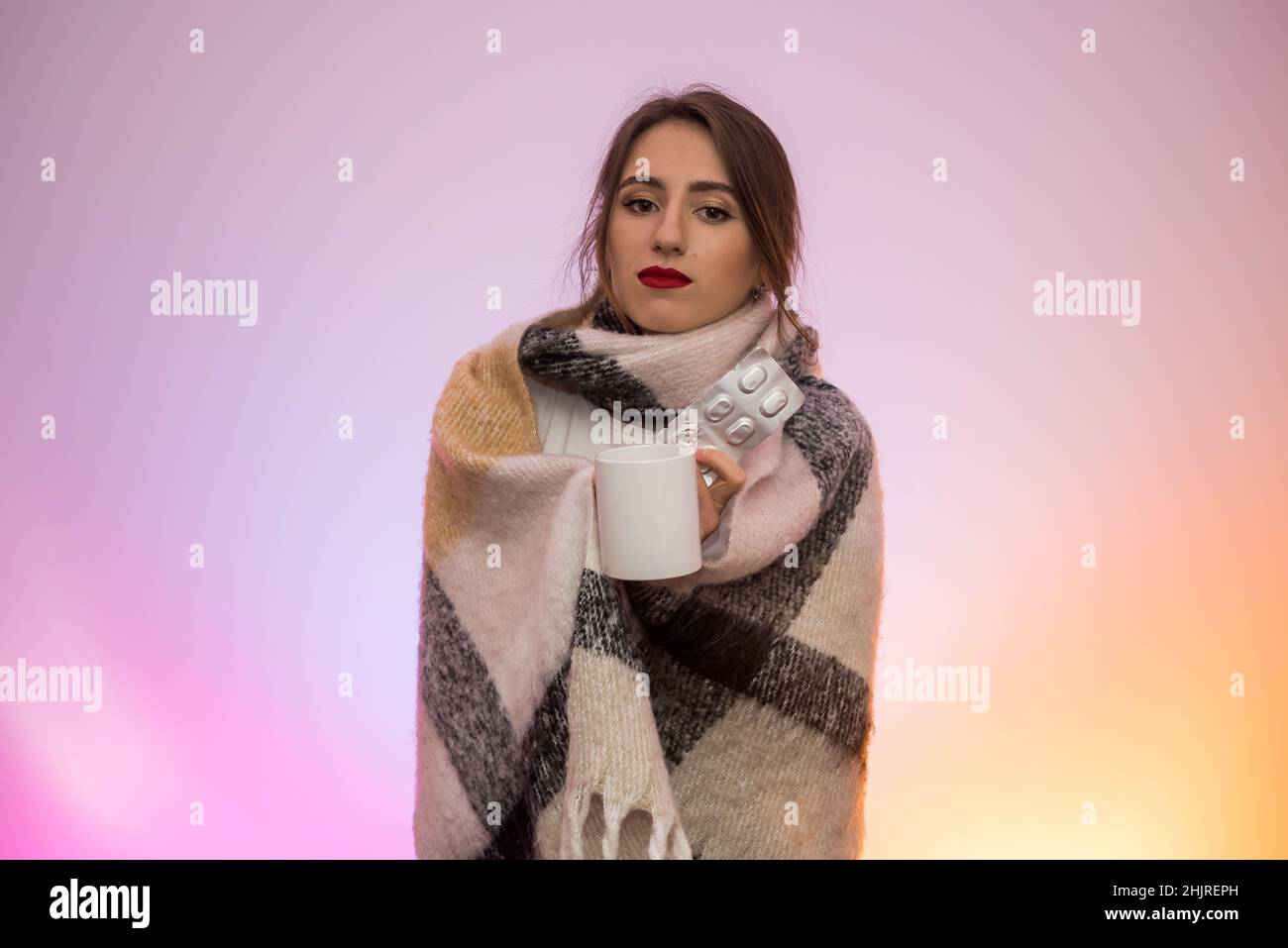 Woman in warm scarf holding pills in blister and having cough. Illness concept Stock Photo