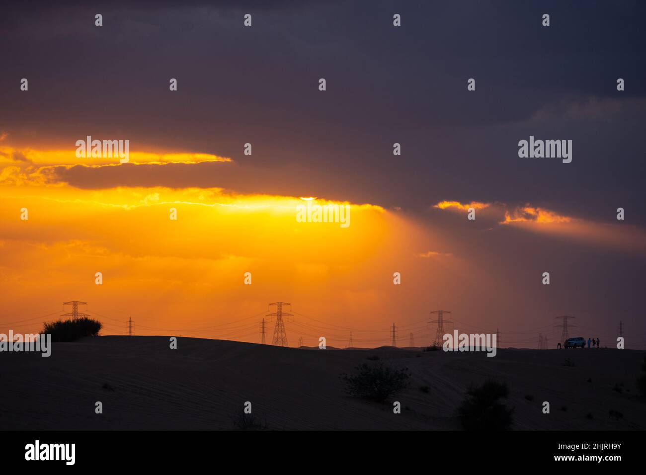 Dramatic desert sunset, sun is coming out from dark clouds, with power line in the background, Dubai, UAE Stock Photo