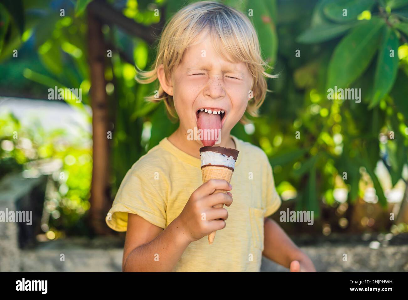 Outdoor portrait of happy boy with ice cream in waffles cone. Cute child holding ice-cream and making gladness face while walking in the park Stock Photo