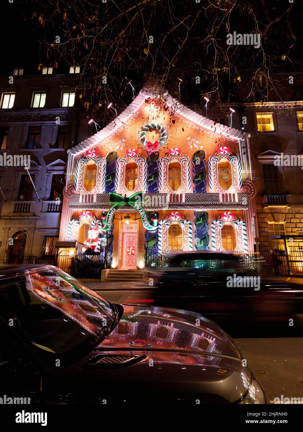 Car drives past Anabel's private club at night with its Christmas Gingerbread House facade in Berkeley Square, London. Stock Photo