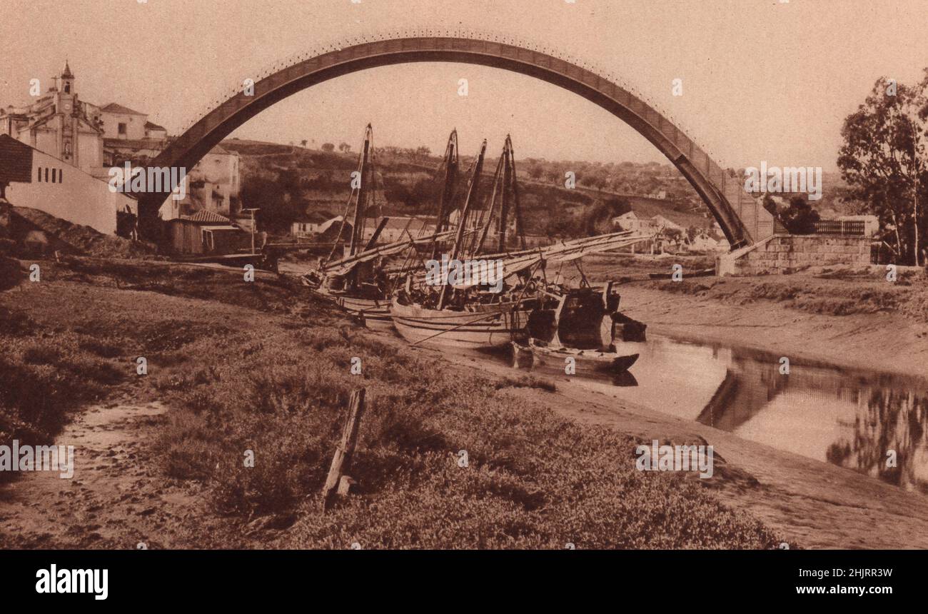 One sailed boats Boats moored to the bank of the Sacavem under the arch of the siphon which sucks the water of the Alviella to Lisbon. Portugal (1923) Stock Photo