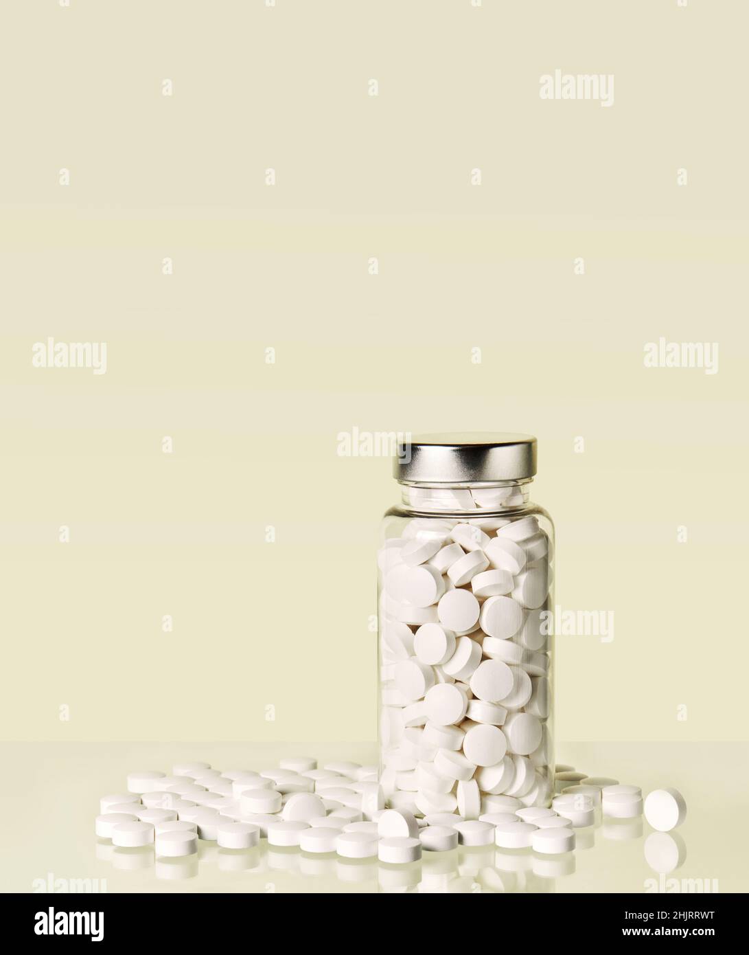 White tablets in a glass jar on the pastel yellow background. Medication in tablets. Copy space Stock Photo