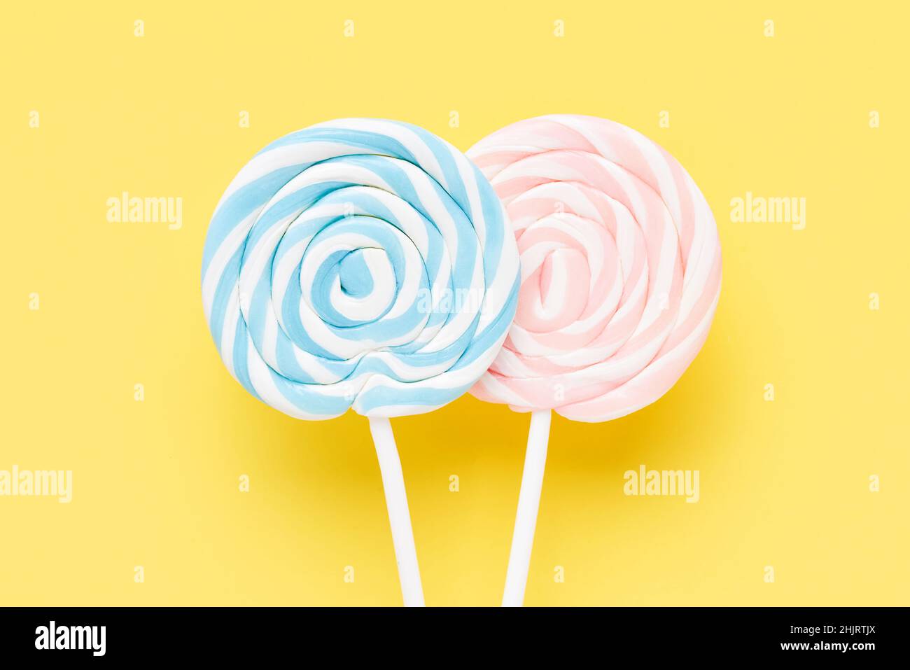 Two colorful lollipops on a white stick on a yellow background. Top view, copy space for text Stock Photo