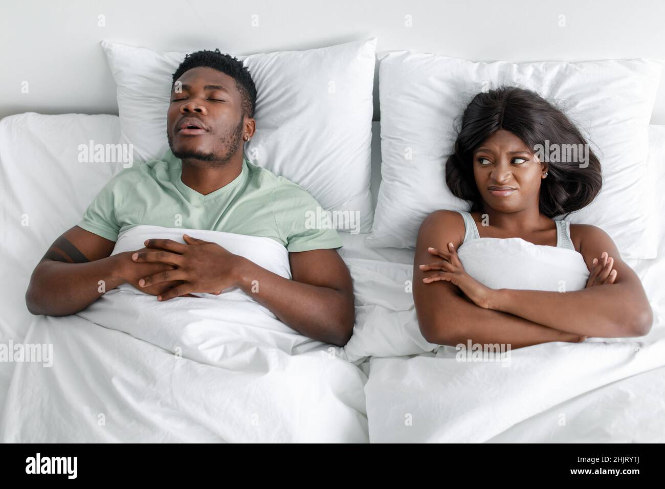 Displeased unhappy millennial african american woman suffers from noise and snoring of sleeping husband on bed Stock Photo