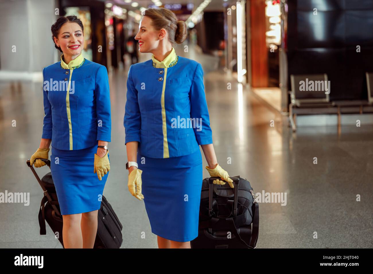 Smiling flight attendants carrying travel bags at airport Stock Photo