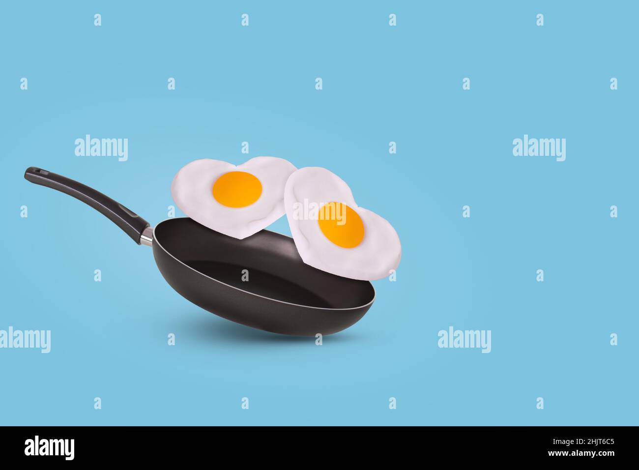 Creative idea with a frying pan and a two fried eggs in heart shape on a bright blue background. Minimal food and love concept. Breakfast idea for Val Stock Photo