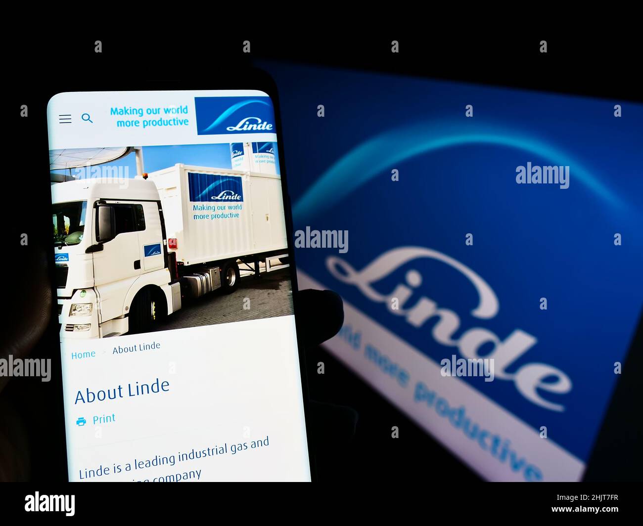 Person holding smartphone with website of chemical company Linde plc on screen in front of business logo. Focus on center of phone display. Stock Photo