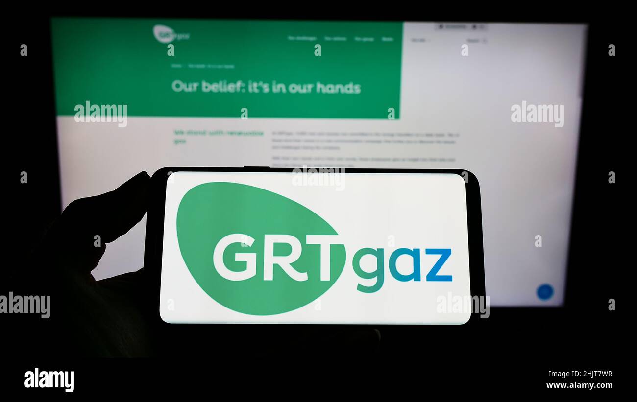 Person holding mobile phone with logo of French natural gas company GRTgaz S.A. on screen in front of business web page. Focus on phone display. Stock Photo