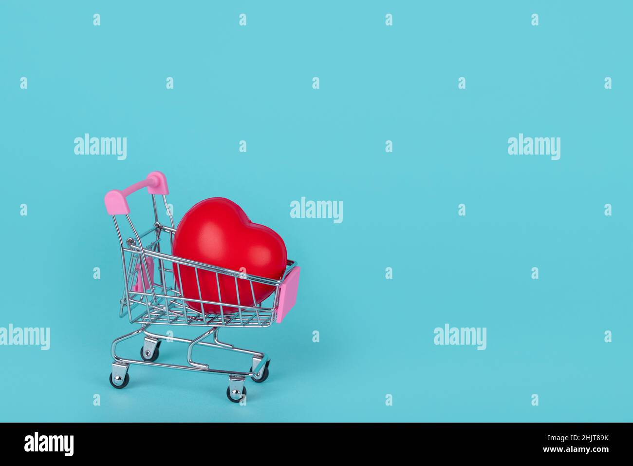 Shopping trolley with red heart on blue background. Creative idea for Valentines, Mothers or International Women's Day shopping and sale. Copy space. Stock Photo