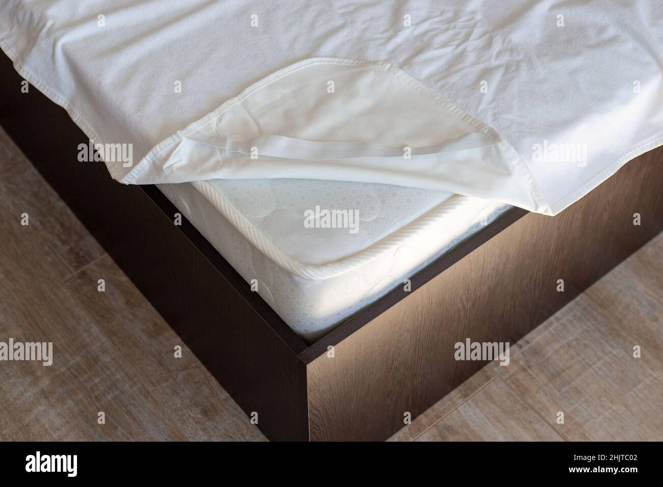 Corner of a wooden bed with a spring mattress and a waterproof mattress topper. Care of home furniture. Stock Photo