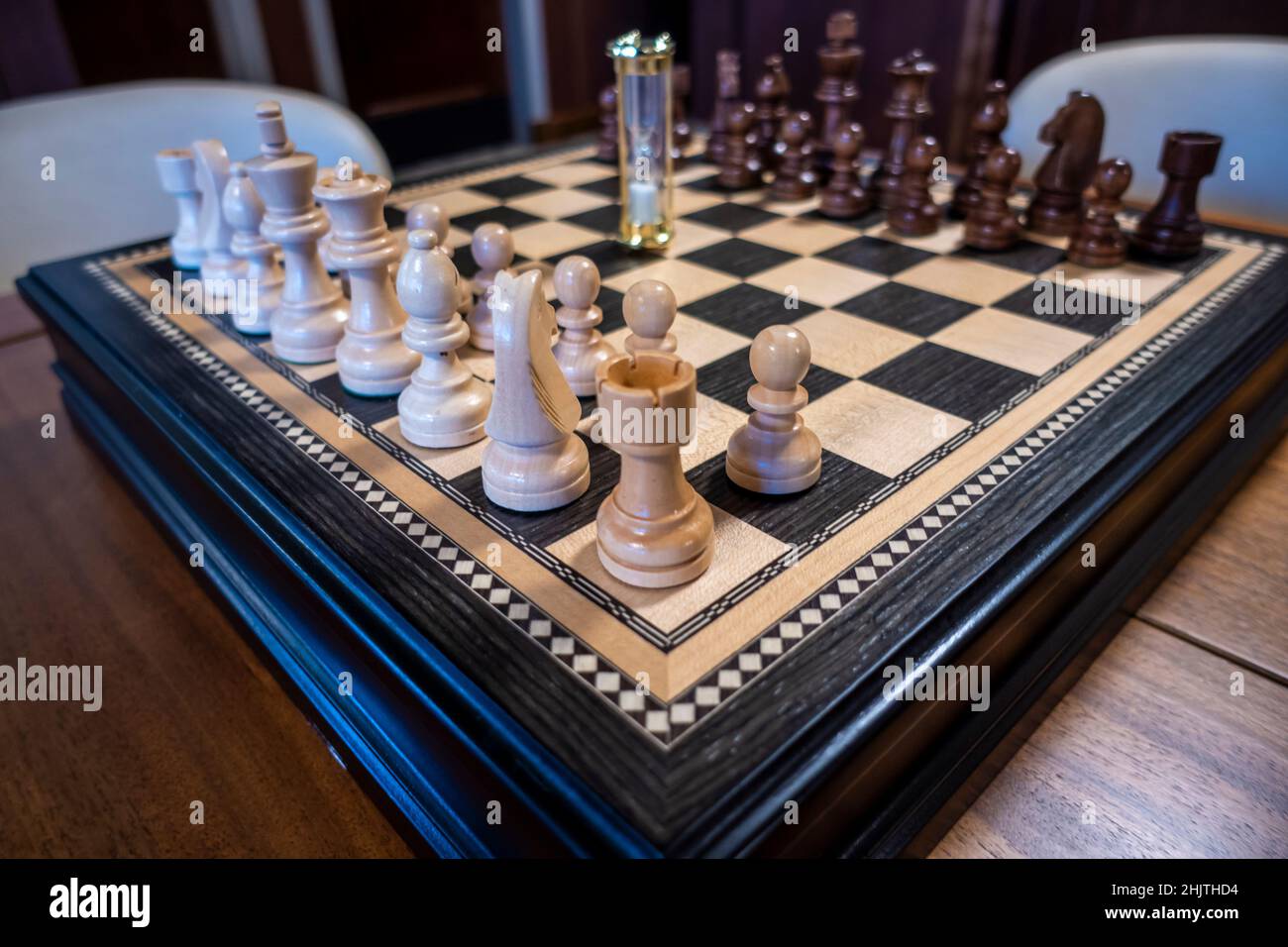 Angled view of a beautiful, wood chess board, with light and dark wood playing pieces, atop a dark wood dining table Stock Photo