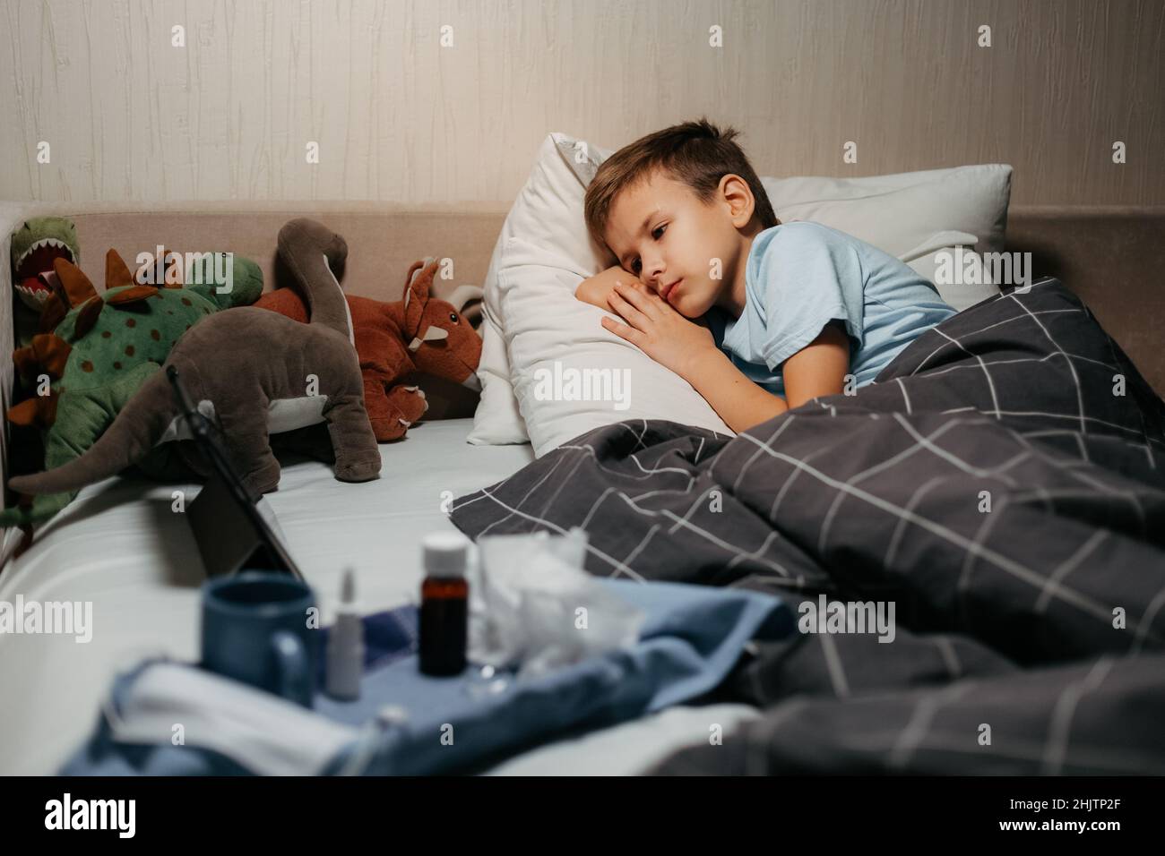 Very sad ill child laying in bed with toys and tablet Stock Photo