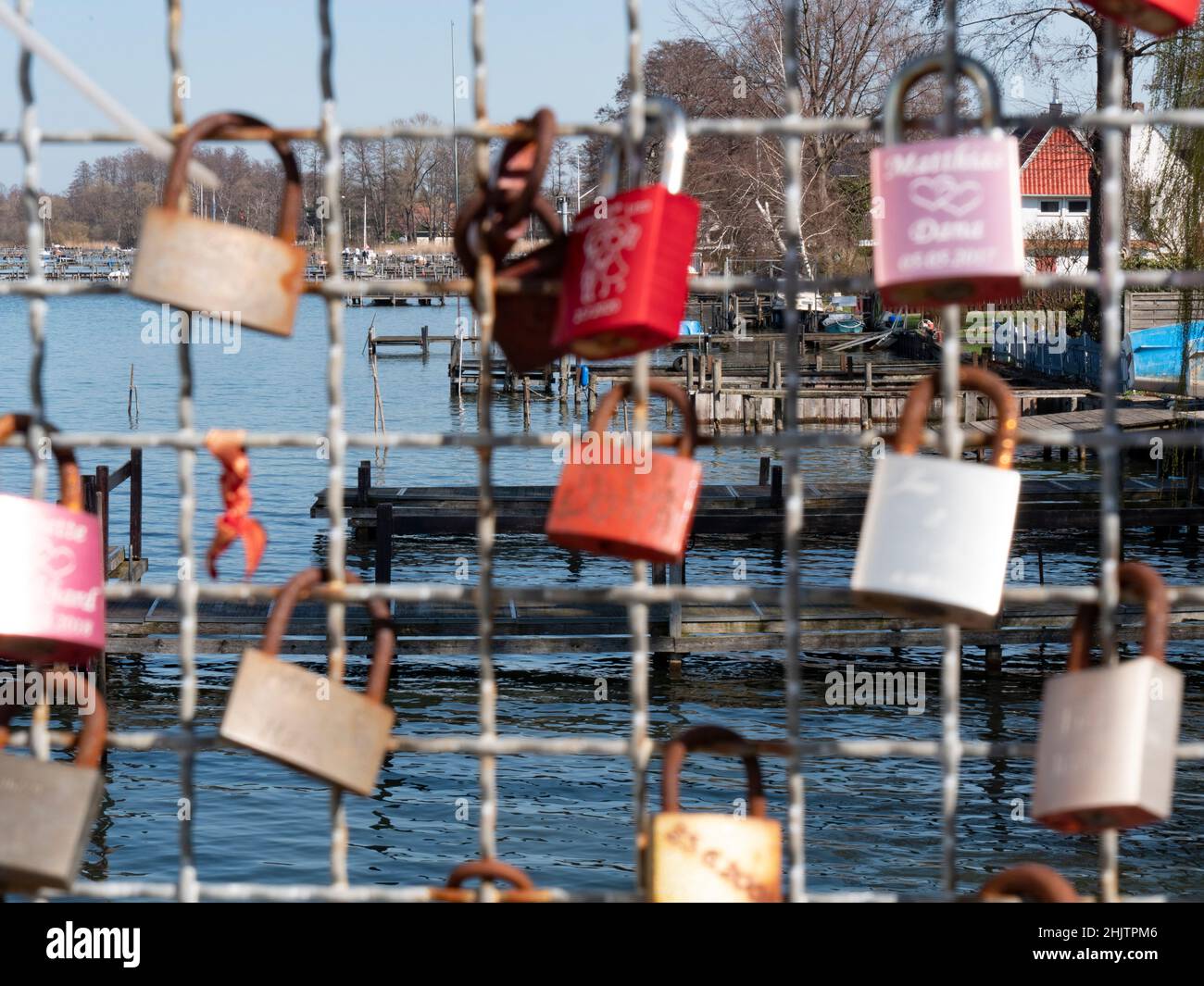 Love locks hang on a grid, in the background is a lake with a marina Stock Photo
