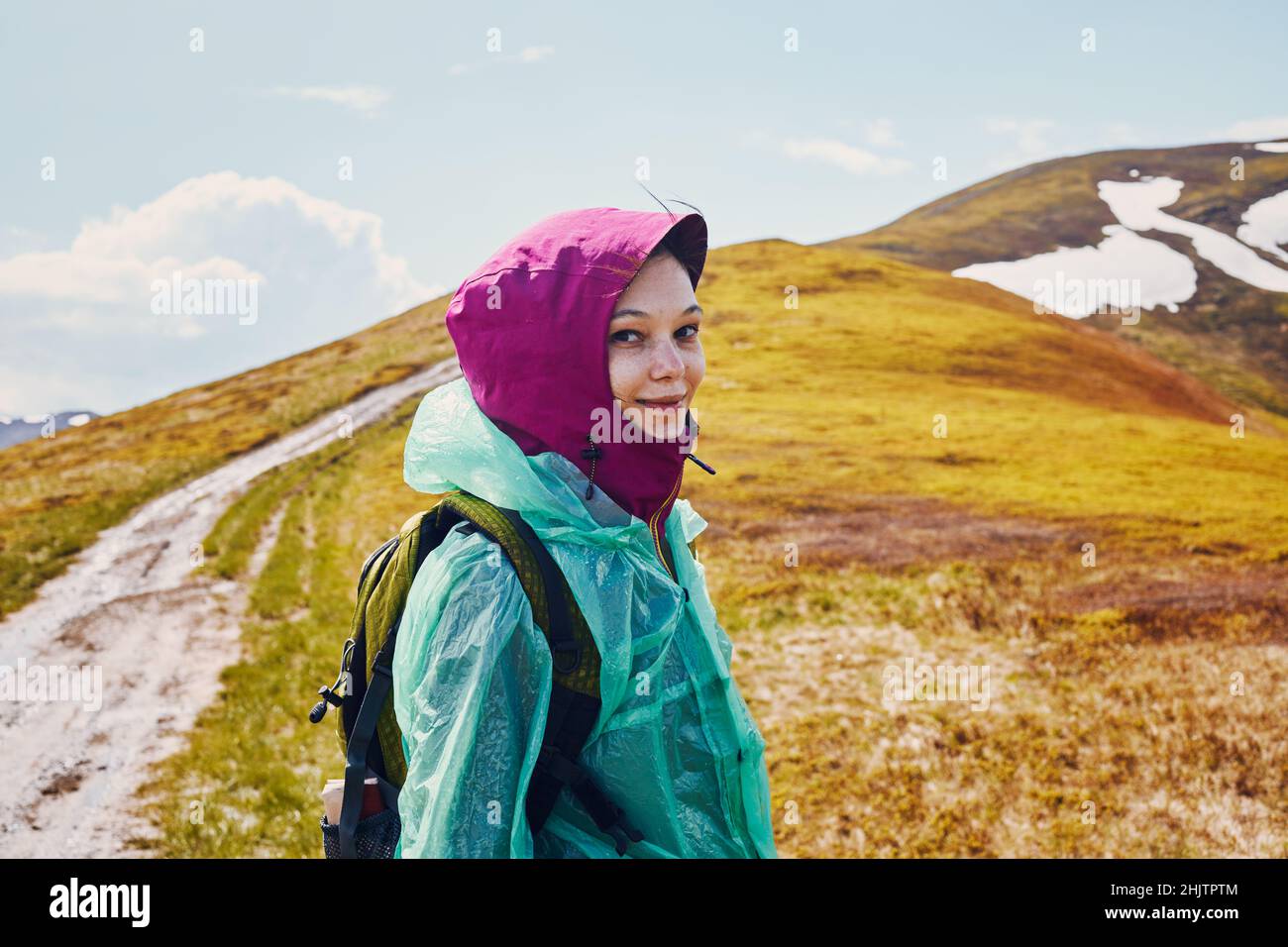 Woman in a raincoat against the backdrop of a mountain peak. Stock Photo