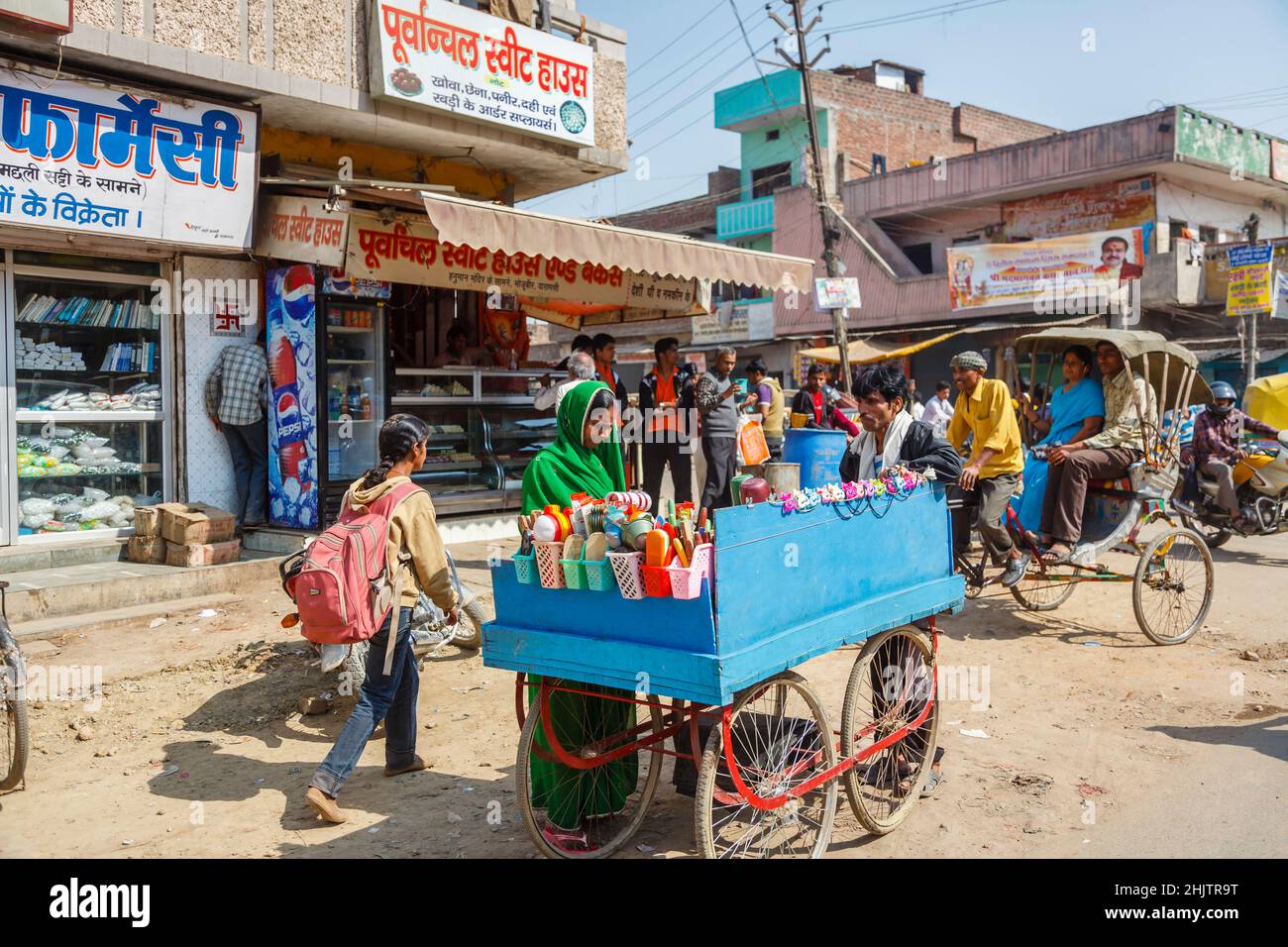 Busy street scene with roadside shops and a barrow selling household goods on the outskirts of Varanasi (formerly Benares), Uttar Pradesh, north India Stock Photo