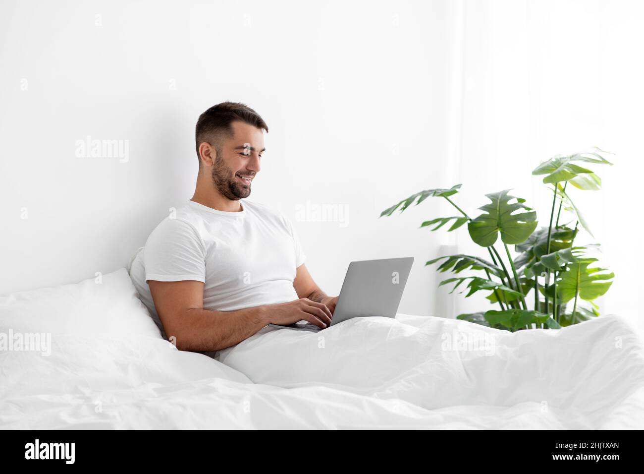 Busy smiling caucasian handsome millennial man in white t-shirt typing ...