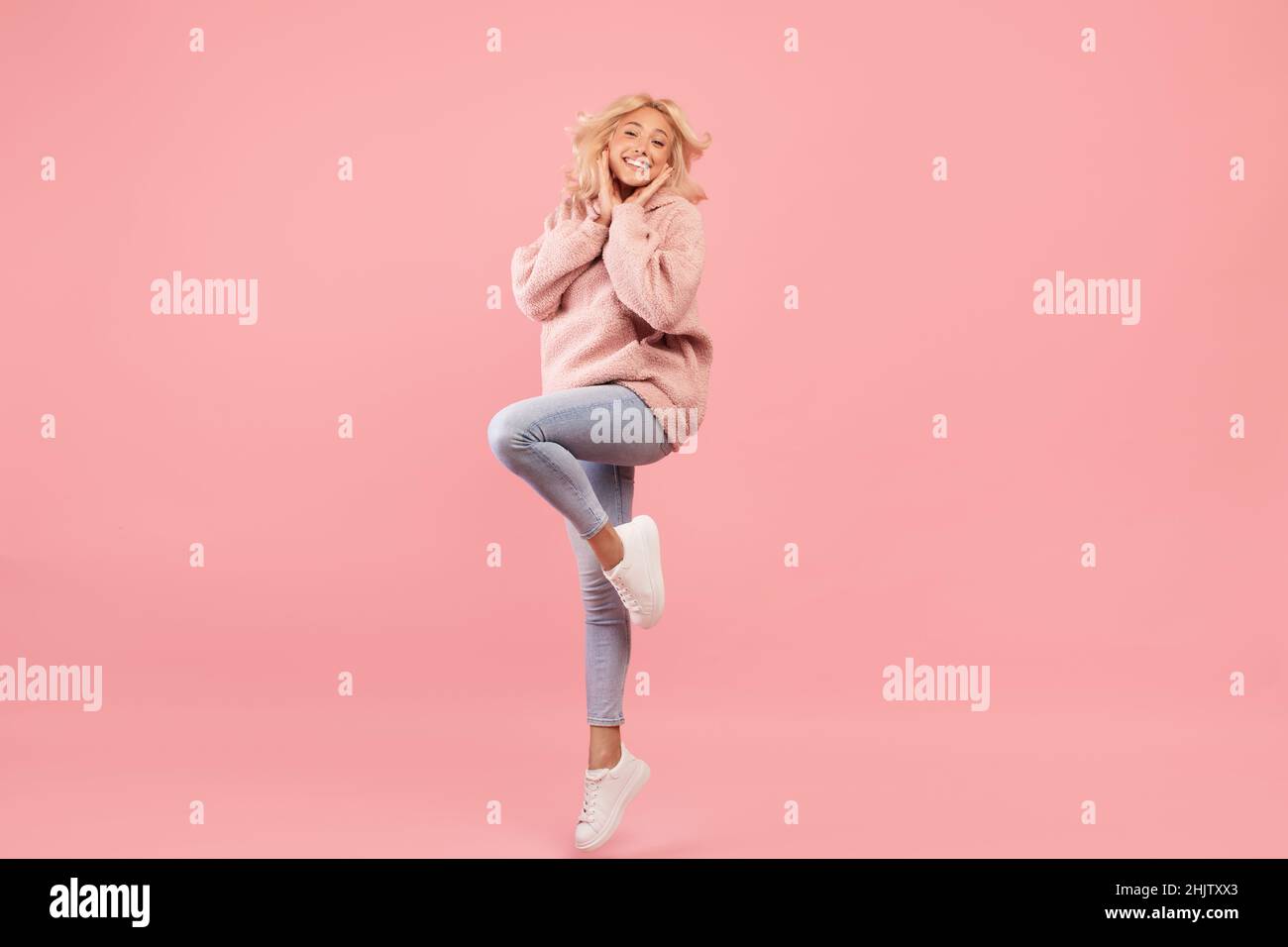 Full body length portrait of playful woman jumping, having fun and smiling at camera, pink background, studio shot Stock Photo