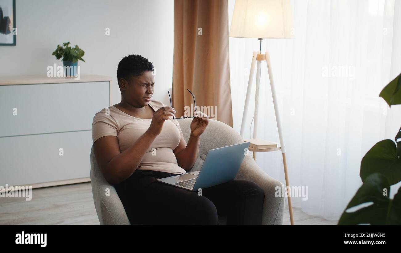 Overwork. Young african american lady suffering from tired eyes, taking off glasses, feeling exhausted of work on laptop Stock Photo